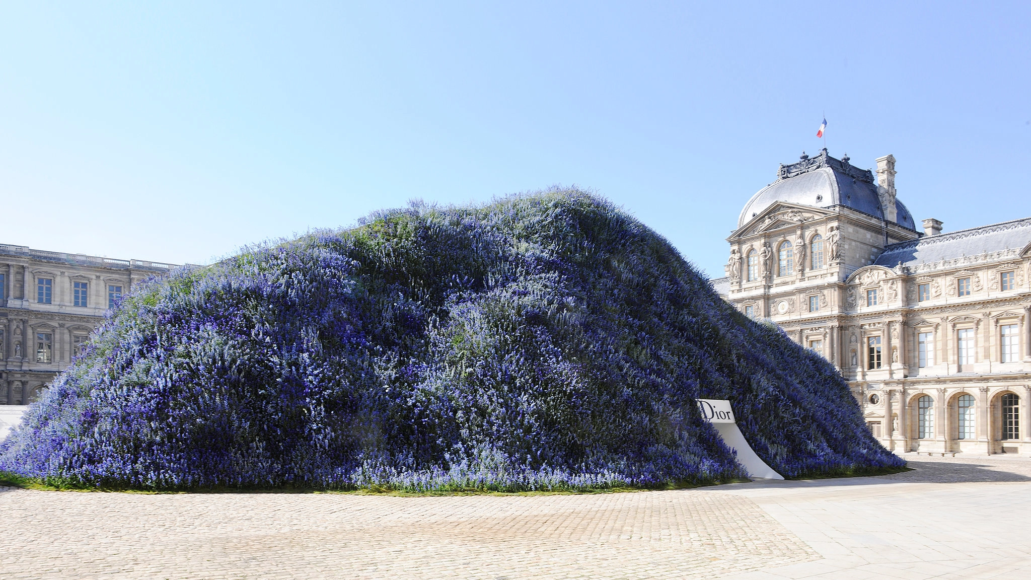 Runway show set inside a floral, moss-covered hill structure built for Christian Dior in the Louvre's Cour Carre courtyard.